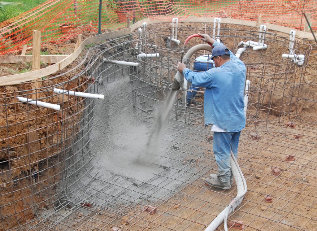 A builder sprays gunite to create a suburban pool